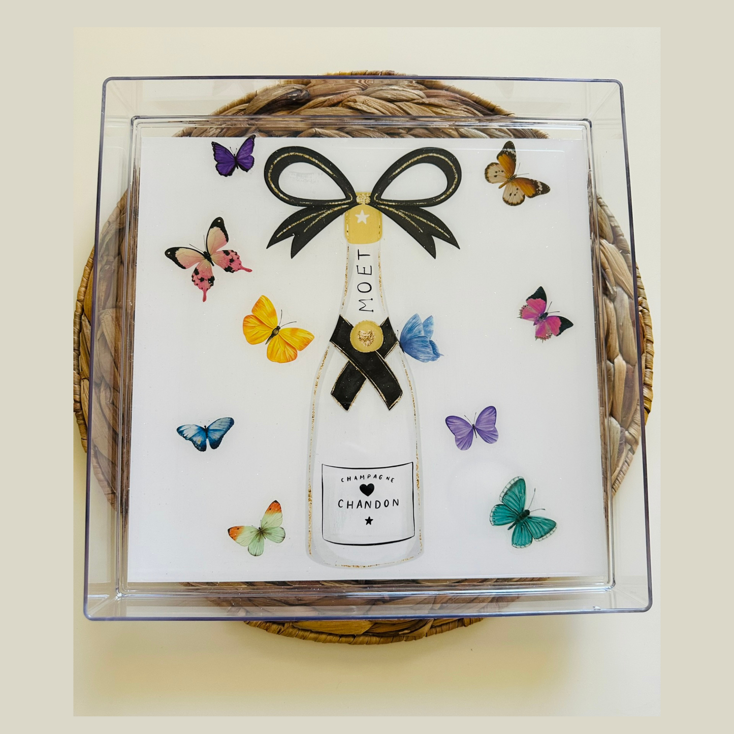 A handmade serving tray with a watercolor painting of a Moet Chandon bottle topped with a black and gold bow, surrounded by colorful butterfly decorations.