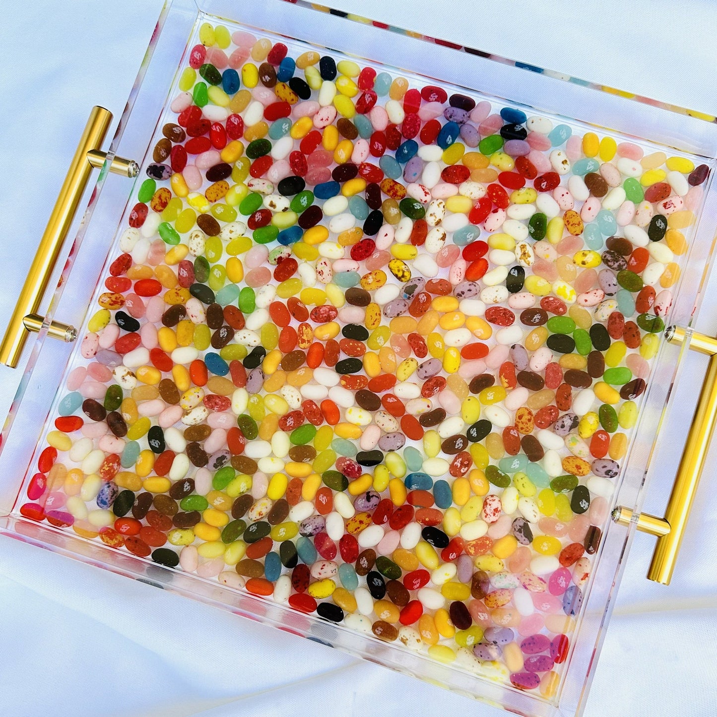An acrylic serving tray filled with multicolored jelly beans, featuring gold handles on the sides.