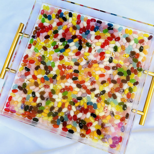 An acrylic serving tray filled with multicolored jelly beans, featuring gold handles on the sides.