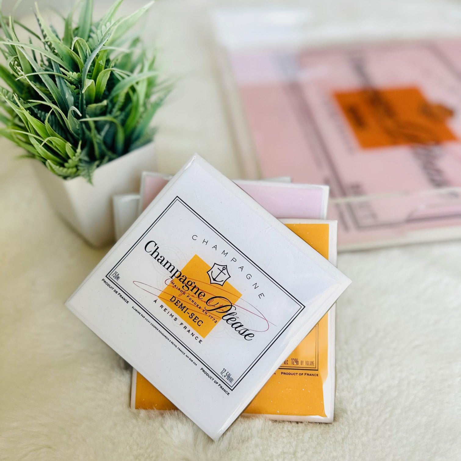 Packaged product with 'Champagne Please' label on a light surface with a plant in the background
